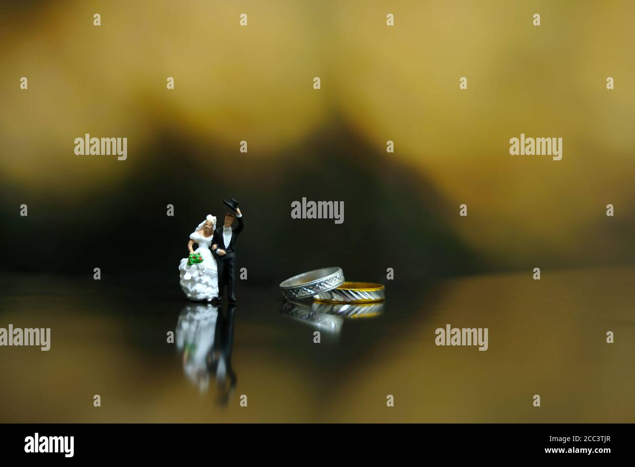 Miniatur Hochzeitskonzept - Braut und Bräutigam laufen auf glänzend Boden neben ihrem goldenen Ehering Stockfoto