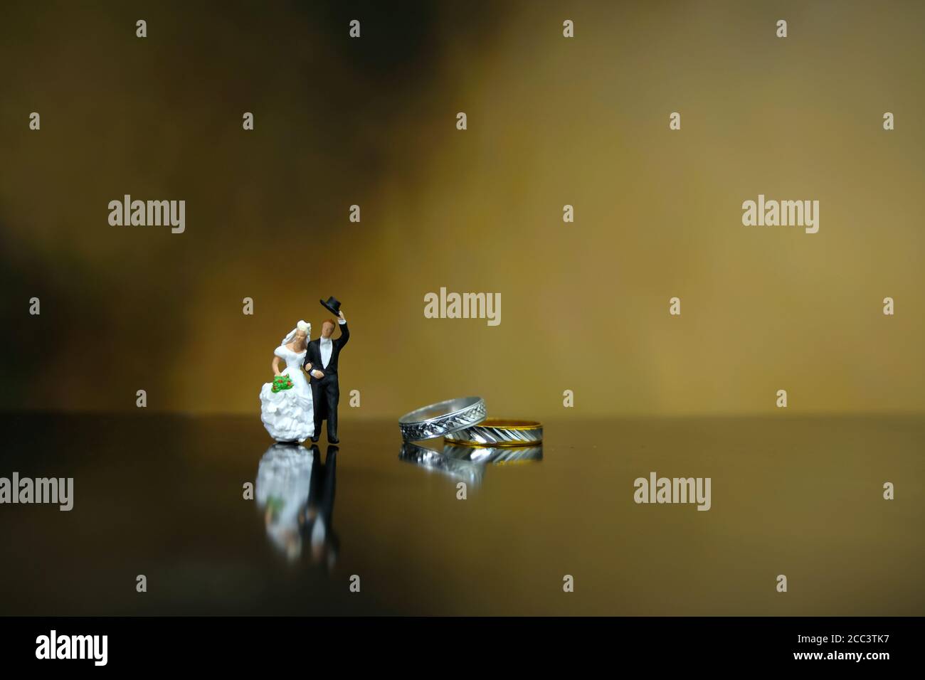 Miniatur Hochzeitskonzept - Braut und Bräutigam laufen auf glänzend Boden neben ihrem goldenen Ehering Stockfoto