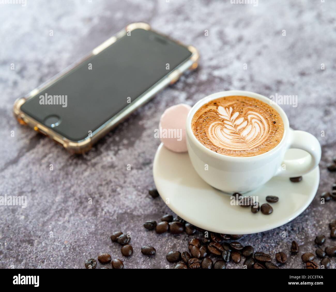 Kaffee auf einem weißen Becher mit einer Untertasse mit Marshmallow, Kaffeebohnen und Handy Hintergrund Weichzeichnen Stockfoto