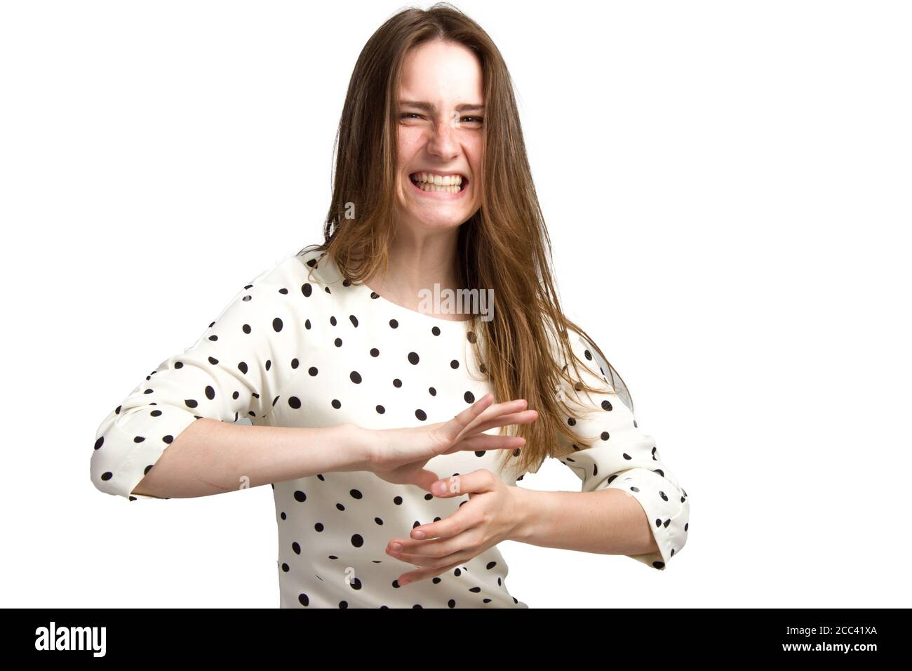 Eine junge Frau mit langen braunen Haaren und einem weißen Polka-Dot-Kleid. Mit einem unzufriedenen, angespannten emotionalen Gesicht. Hält seine Hände horizontal parallel zur Handfläche vor ihm. Isoliert auf Weiß Stockfoto