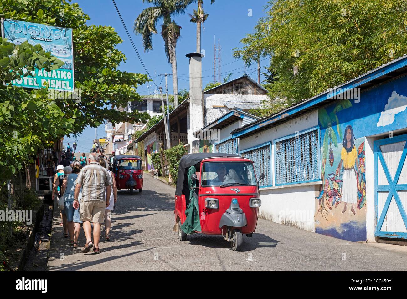 Westliche ältere Touristen und rot gefärbte Tuk-Tuks / Mototaxis in der Straße in der Stadt Livingston, Izabal Department, Guatemala, Mittelamerika Stockfoto Westliche ältere Touristen und rot gefärbte Tuk-Tuks / Mototaxis in der Straße in der Stadt Livingston, Izabal Department, Guatemala, Mittelamerika Stockfoto
