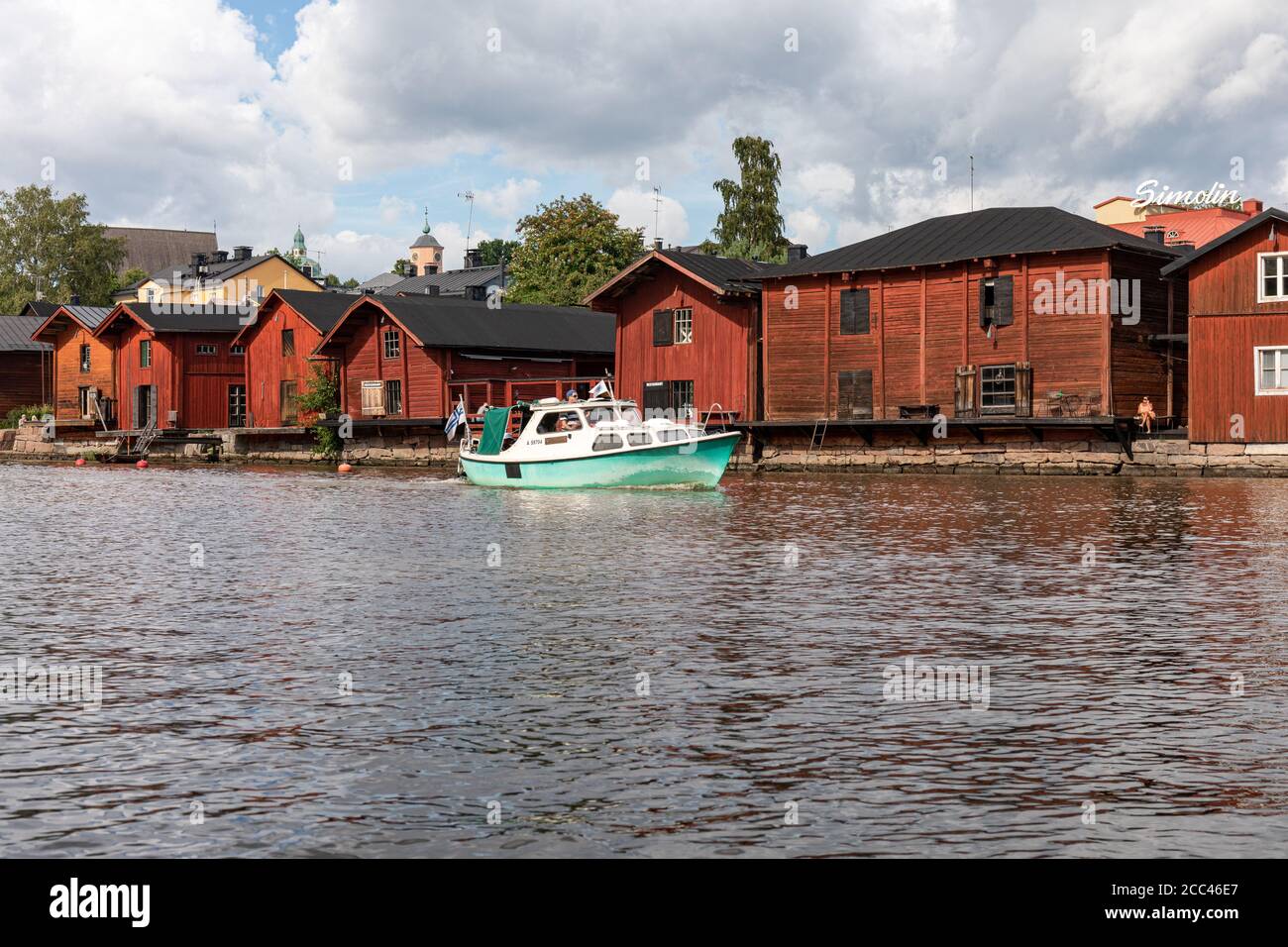 Hellgrünes Motorboot, das an den Holzlagerhäusern der Altstadt im Fluss Porvoonjoki in Porvoo, Finnland, vorbeifährt Stockfoto