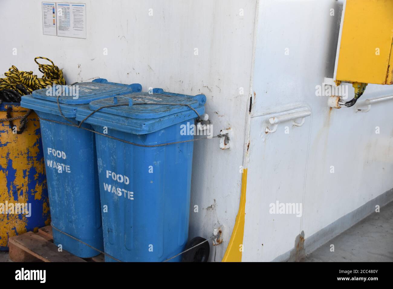 Blaue Kunststoffabfallbehälter für Lebensmittelabfälle, die fest am Geländer sitzen, befinden sich hinter dem Überbau des Containerschiffes. Stockfoto