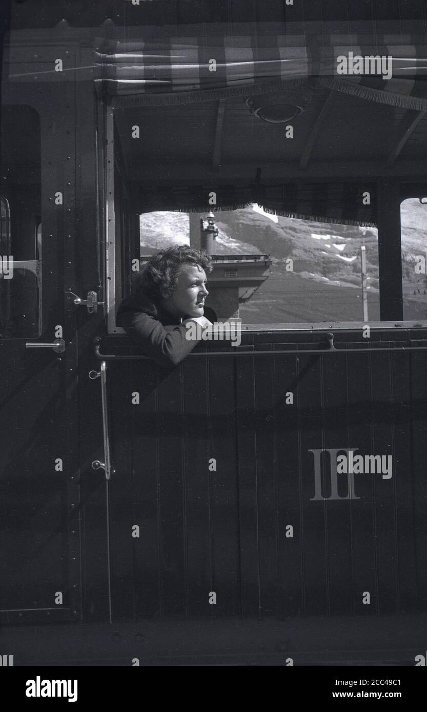 1950s, historisch, eine Frau, die in einem Schweizer Bergbahnwagen sitzt und sich aus einem offenen Fenster lehnt, Schweizer Alpen, Schweiz. Die Zahl 3 in römischen Ziffern ist in Buchstaben auf dem Waggon do Stockfoto