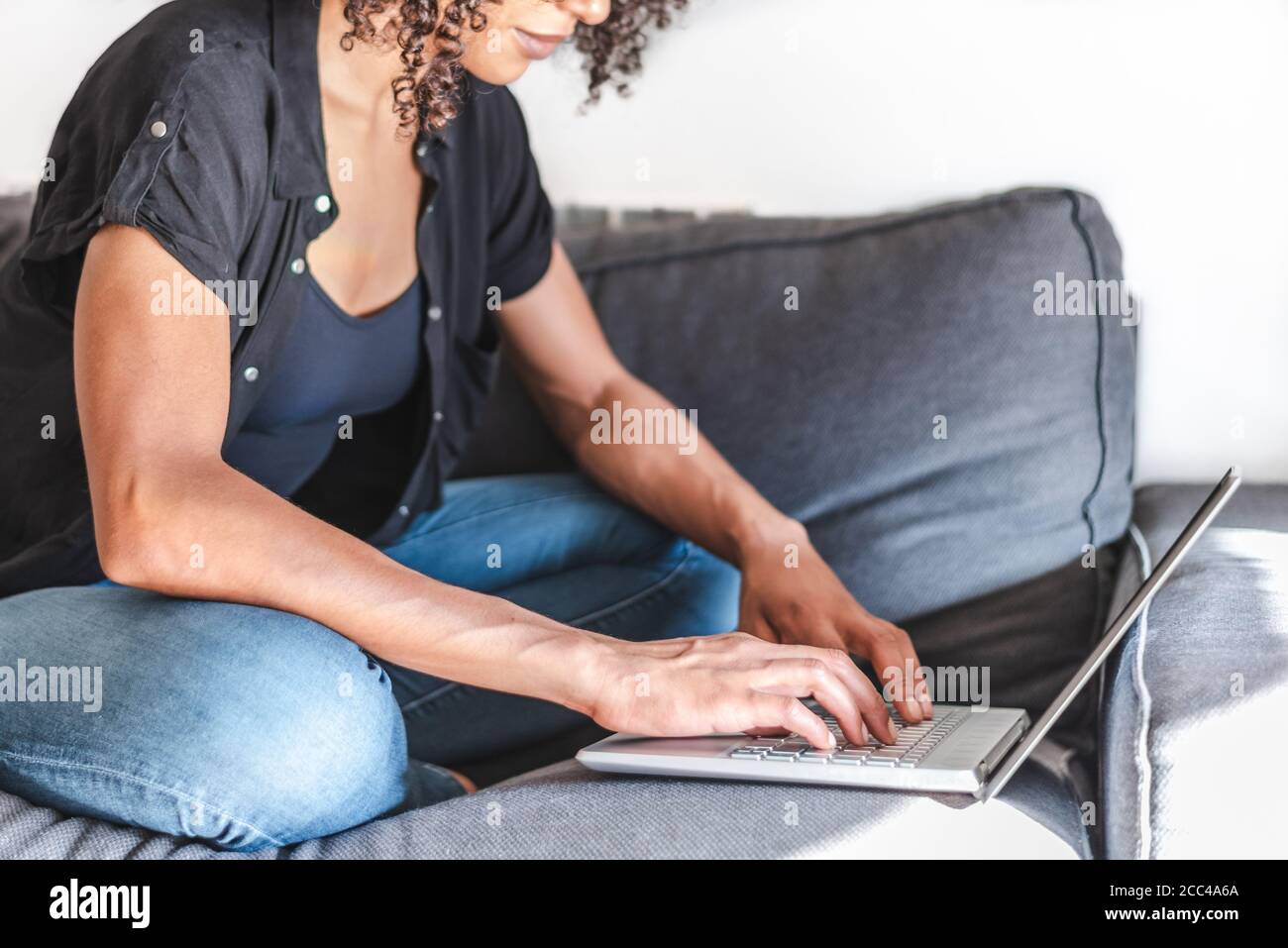 Schwarze Afro-Frau mit einem modernen Laptop auf einem grauen Sofa. Selektiver Fokus auf Hände und Laptop Stockfoto