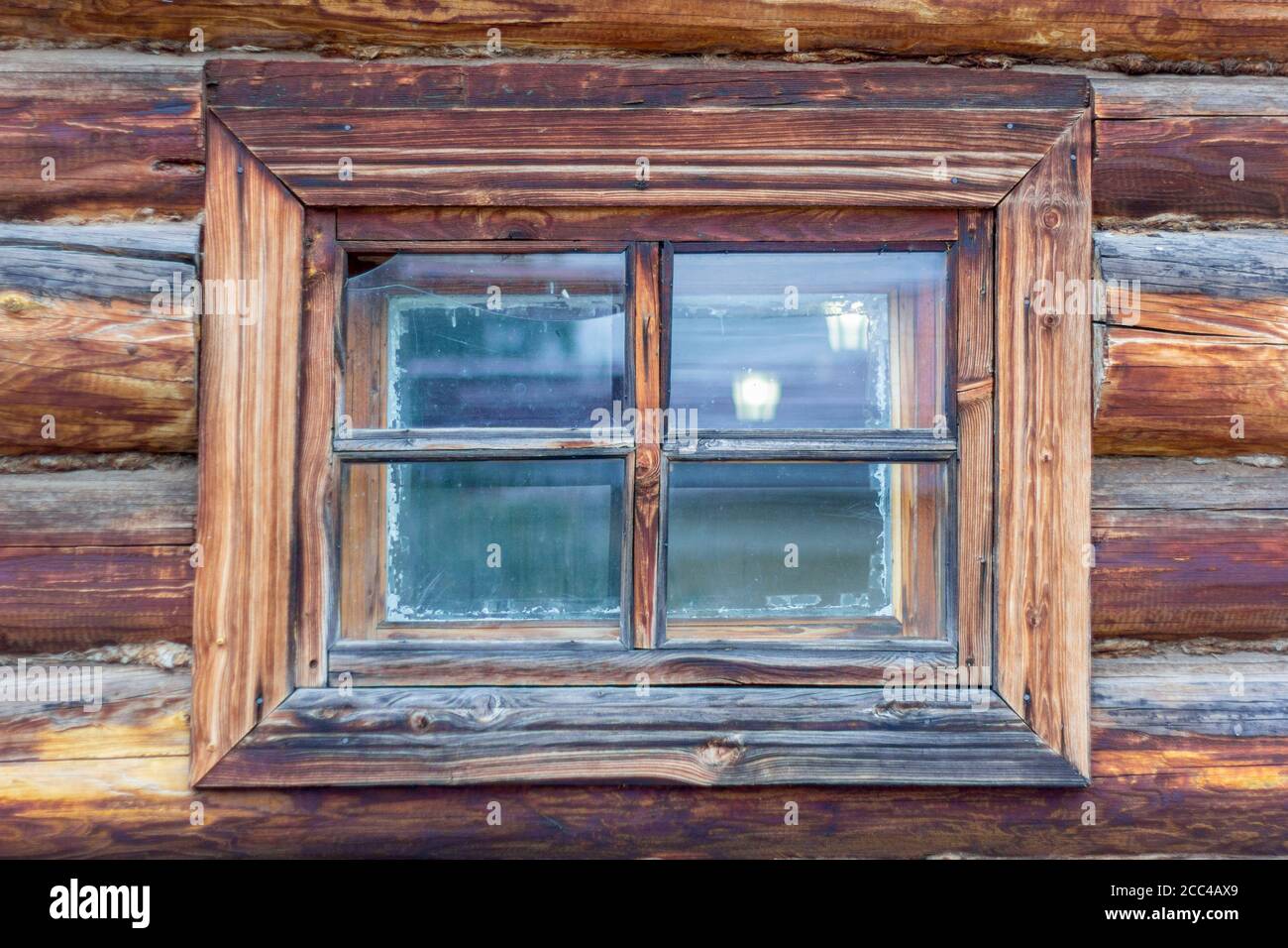 Ein Fragment einer alten Holzhütte mit einem Fenster. Ein altes kleines Fenster mit Rissen in einer alten Holzhütte. Stockfoto