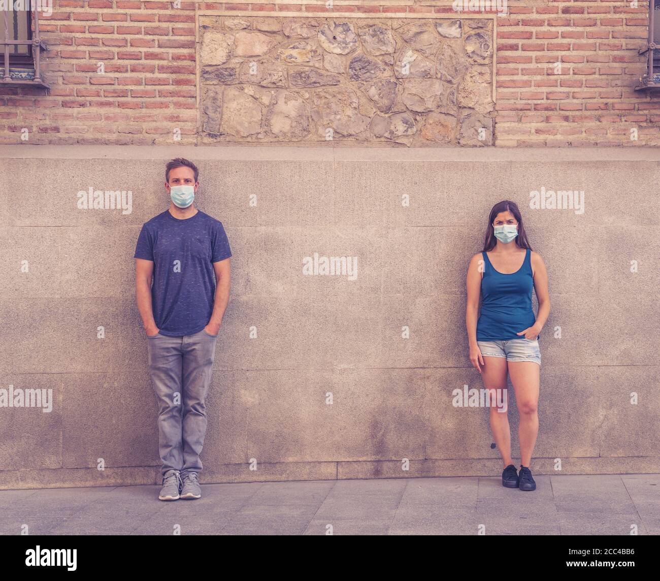 Mann und Frau tragen schützende Gesichtsmasken, die 2 m voneinander entfernt stehen und soziale Distanz halten, um die Ausbreitung des Coronavirus zu vermeiden. Konzeptionelle imag Stockfoto