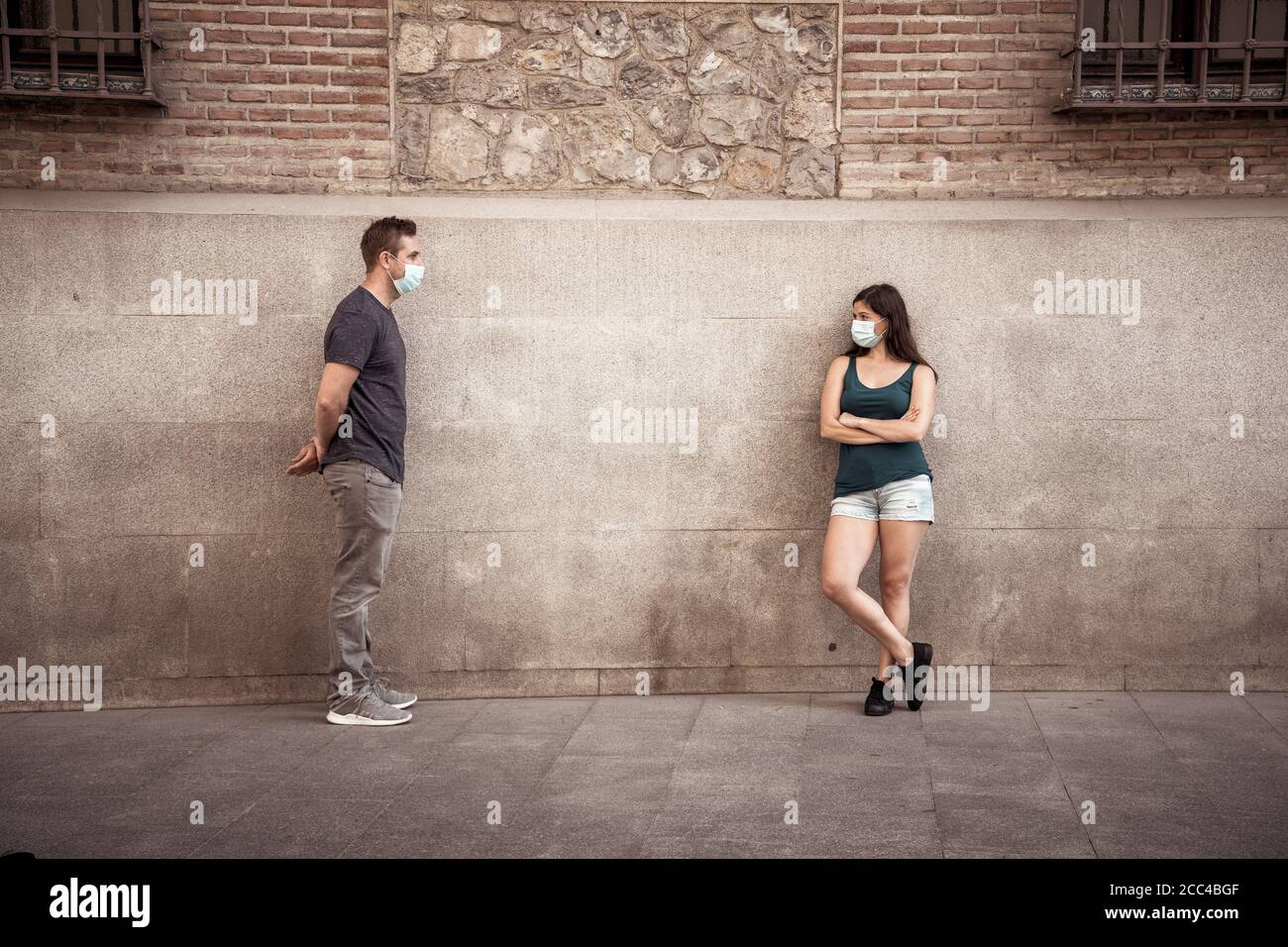 Mann und Frau tragen schützende Gesichtsmasken, die 2 m voneinander entfernt stehen und soziale Distanz halten, um die Ausbreitung des Coronavirus zu vermeiden. Konzeptionelle imag Stockfoto