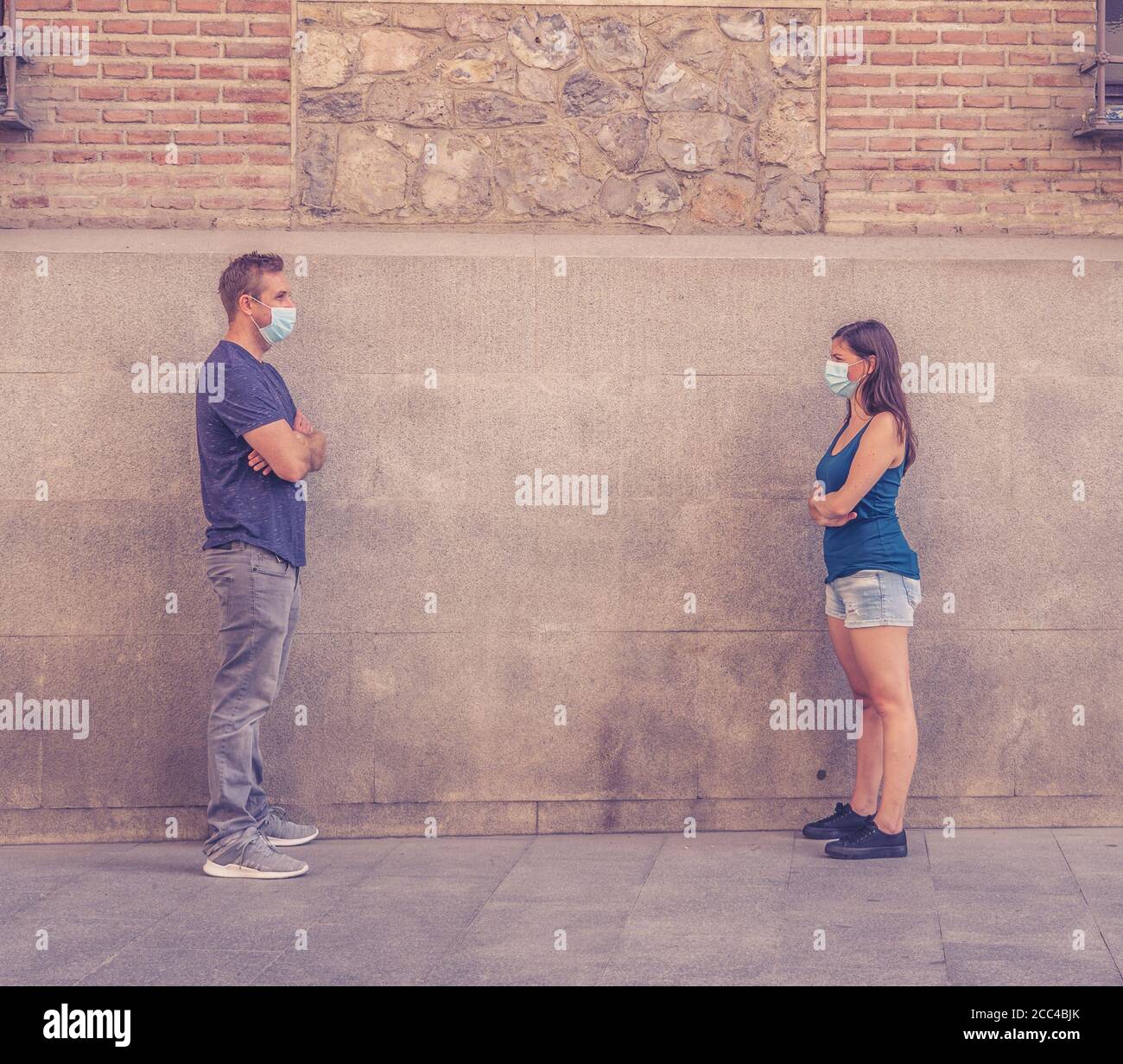 Mann und Frau tragen schützende Gesichtsmasken, die 2 m voneinander entfernt stehen und soziale Distanz halten, um die Ausbreitung des Coronavirus zu vermeiden. Konzeptionelle imag Stockfoto