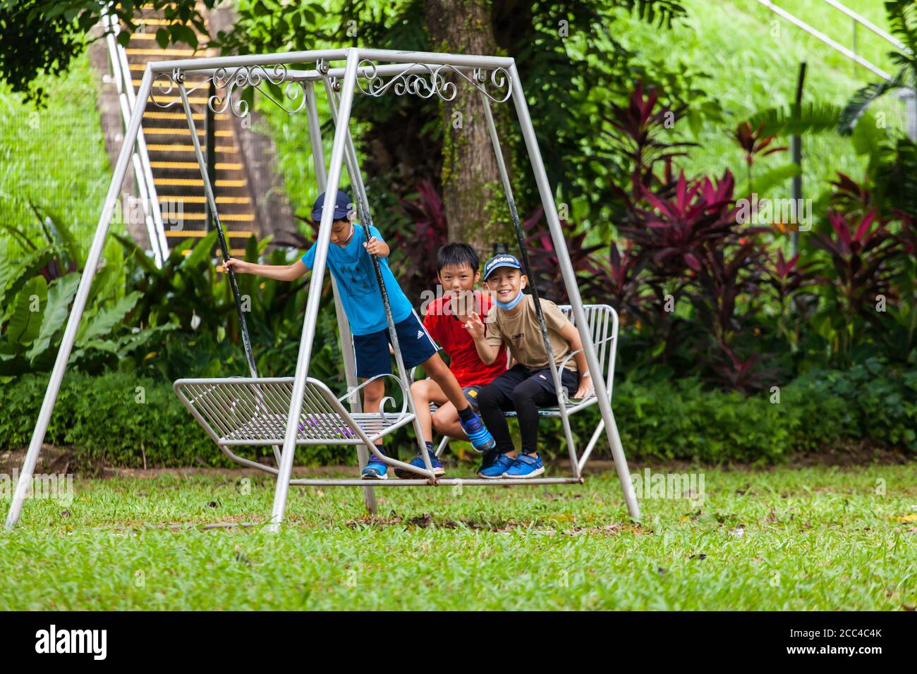 Ein Junge steht, um kinetische Energie zu verwenden, um eine Outdoor-Schaukel mit seinen Freunden zu schwingen, die hinter sitzen. Stockfoto