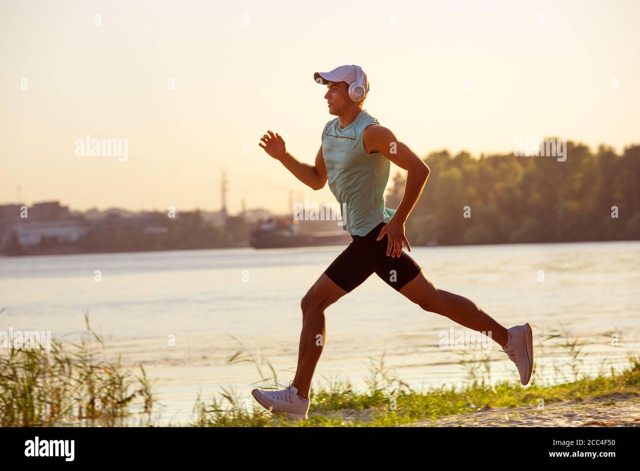 Laufen, Joggen. Ein junger Sportler, der draußen am Flussufer trainieren und Musik hören kann. Konzept für einen gesunden Lebensstil, Wellness, Sport, Aktivität, Gewichtsverlust. Inspiriert von der Natur, Sommerzeit. Stockfoto
