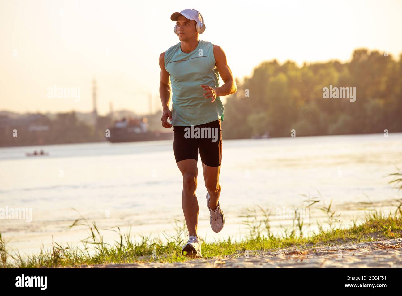 Laufen, Joggen. Ein junger Sportler, der draußen am Flussufer trainieren und Musik hören kann. Konzept für einen gesunden Lebensstil, Wellness, Sport, Aktivität, Gewichtsverlust. Inspiriert von der Natur, Sommerzeit. Stockfoto