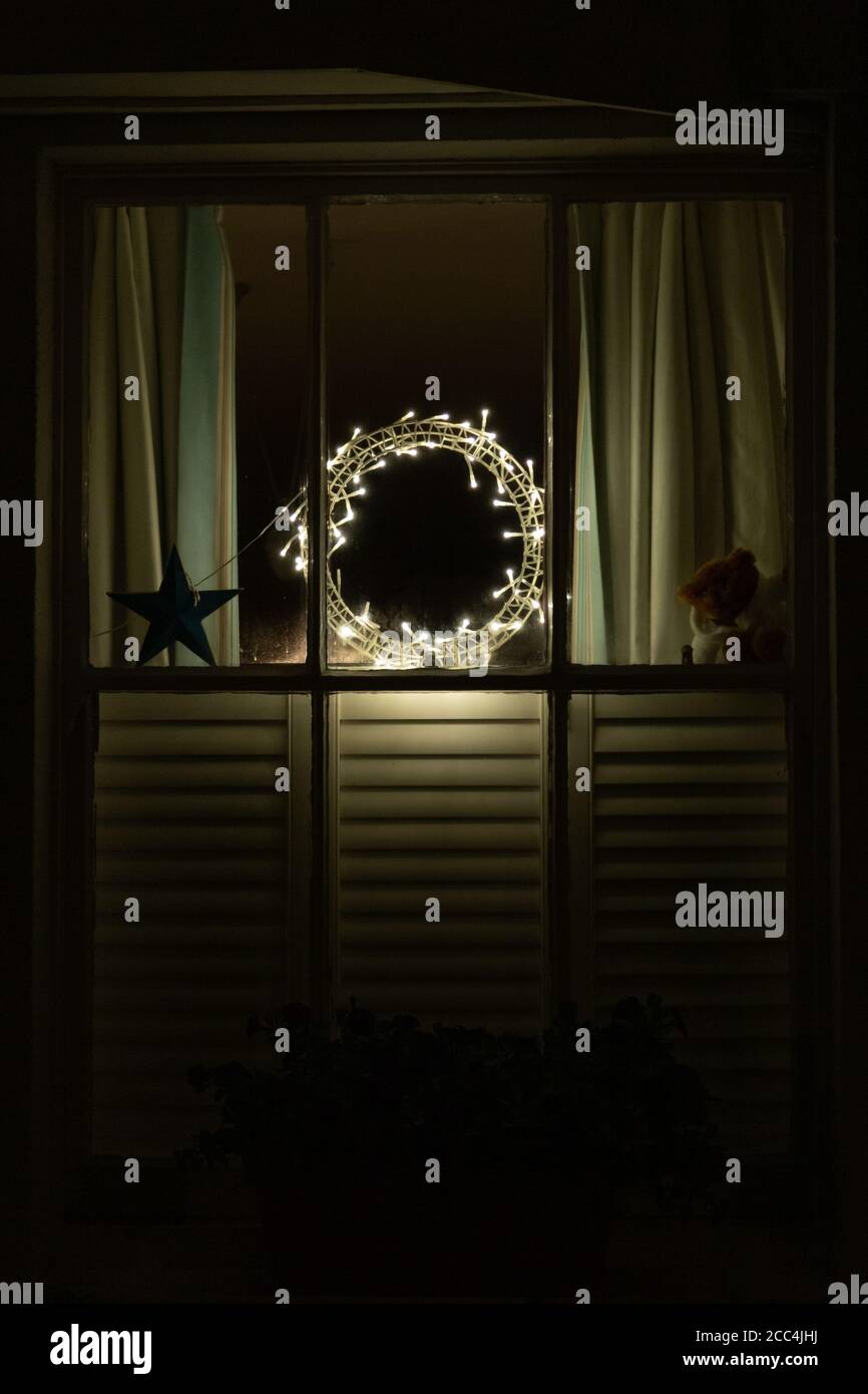 Ein gemütlich aussehendes Fenster eines Hauses mit einem Teddy Tragen Sie im Fenster mit einem Kranz aus Lichtern Stockfoto