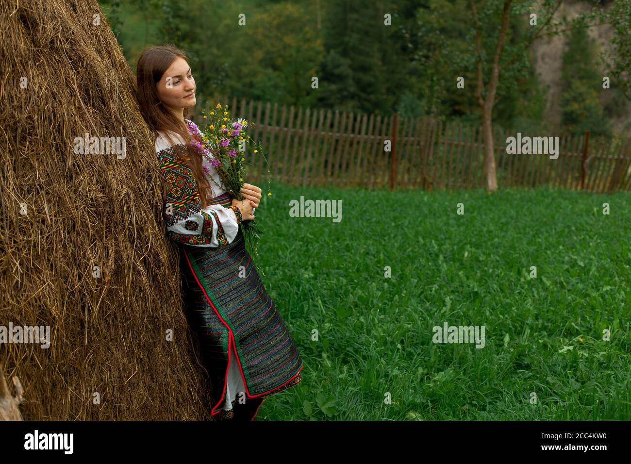 Mädchen mit lockeren Haaren mit einem Blumenstrauß steht Bei einem Heuhaufen Stockfoto