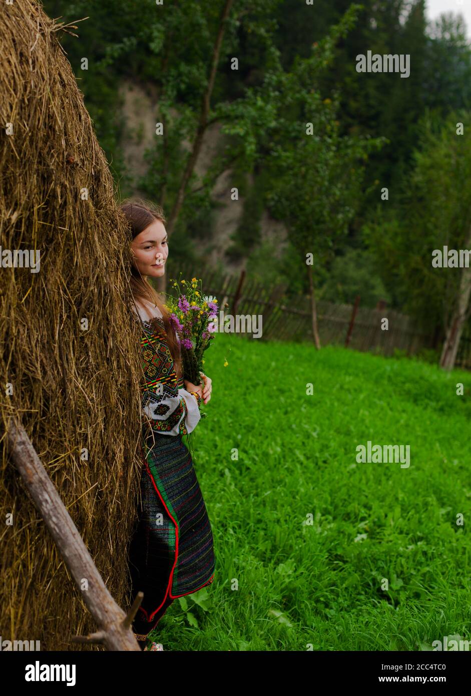 Mädchen mit lockeren Haaren mit einem Blumenstrauß steht Bei einem Heuhaufen Stockfoto