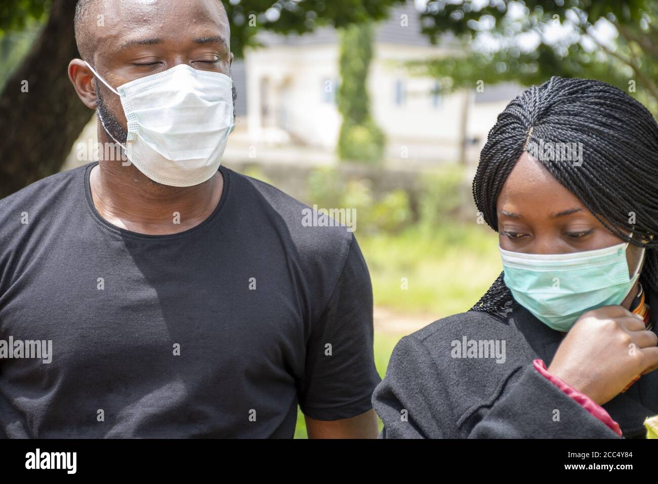 Flacher Fokus von zwei afrikanischen Menschen mit Gesichtsmasken und Blumen Trauer auf einem Friedhof Stockfoto