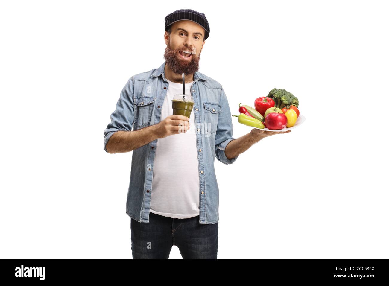 Fröhlicher bärtiger Kerl mit einem grünen Smoothie und einem Teller Von frischem Obst und Gemüse isoliert auf weißem Hintergrund Stockfoto