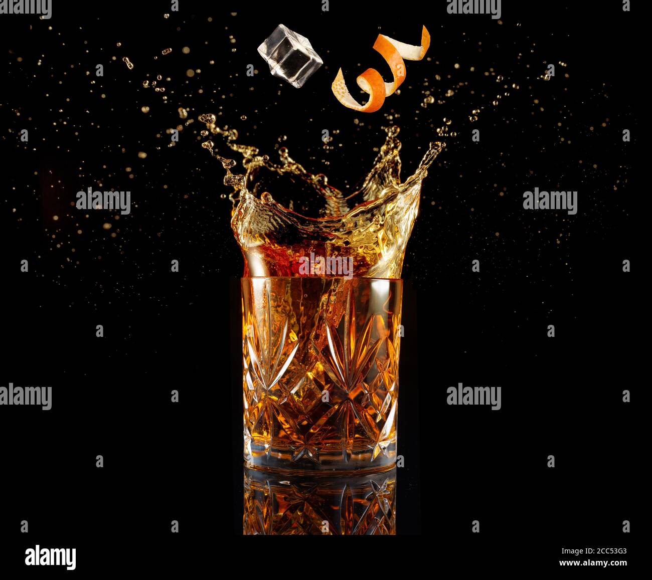 Orangenschale und Eis fallen in spritzendem Cocktail isoliert auf Schwarz Stockfoto