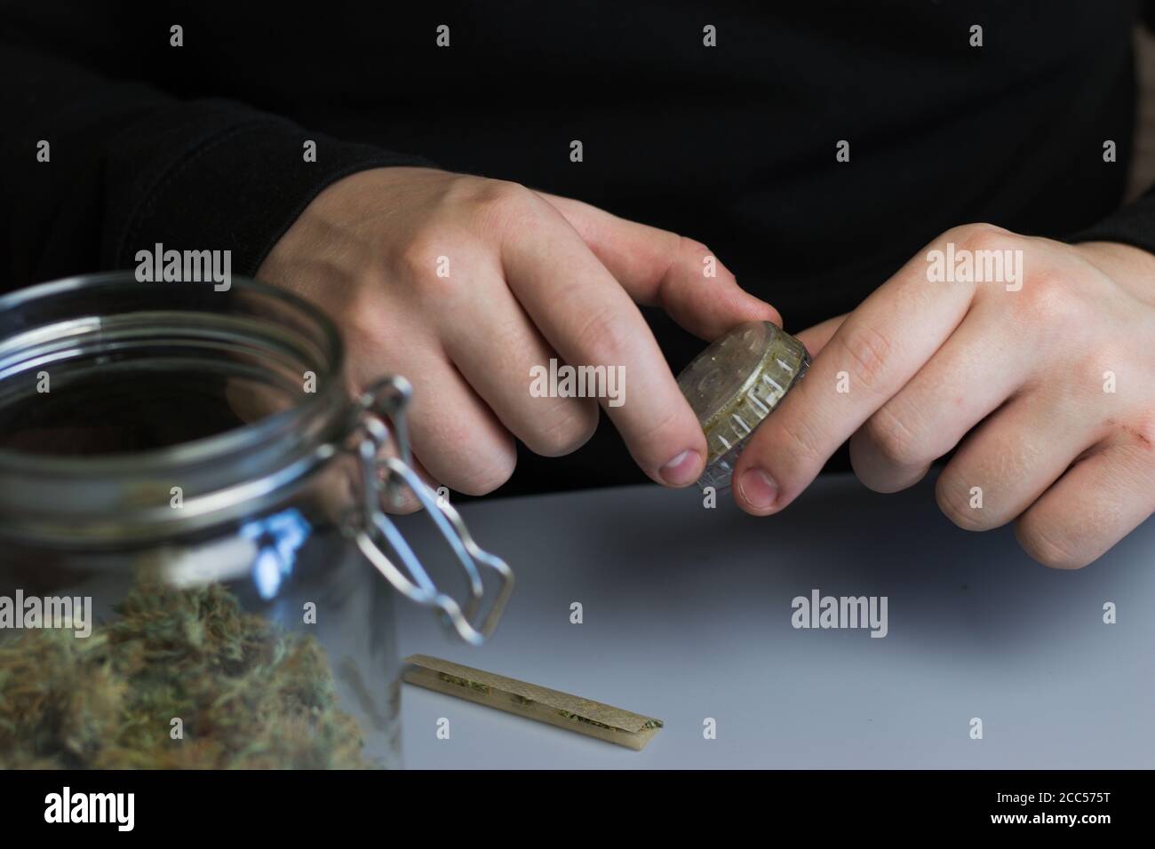Mann, der Grinder mit Cannabis verwendet. Prozess des Marihuanakonsums Stockfoto