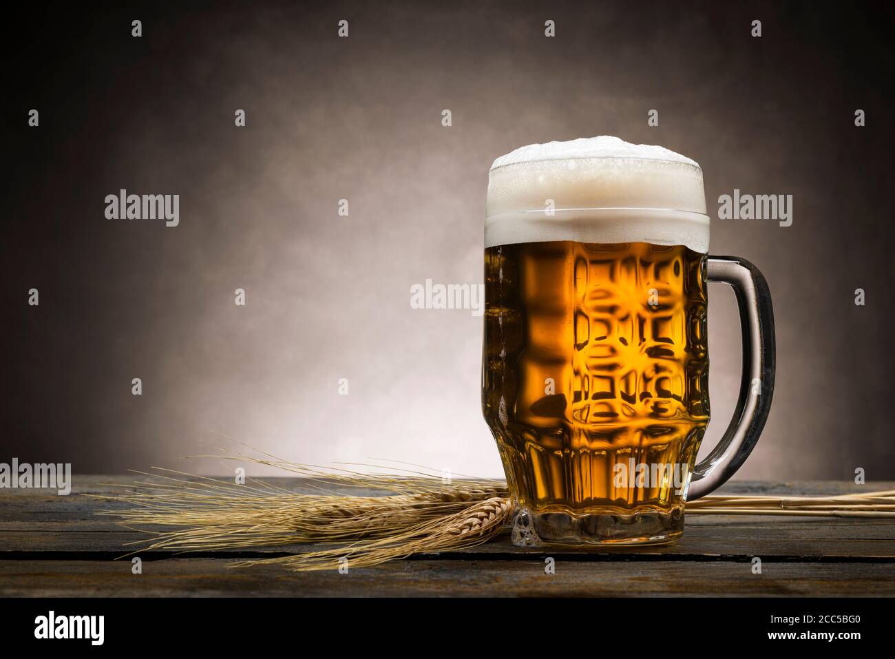Pint blondes Bier mit Schaum auf Holztisch, mit Ähren aus Weizen. Stockfoto