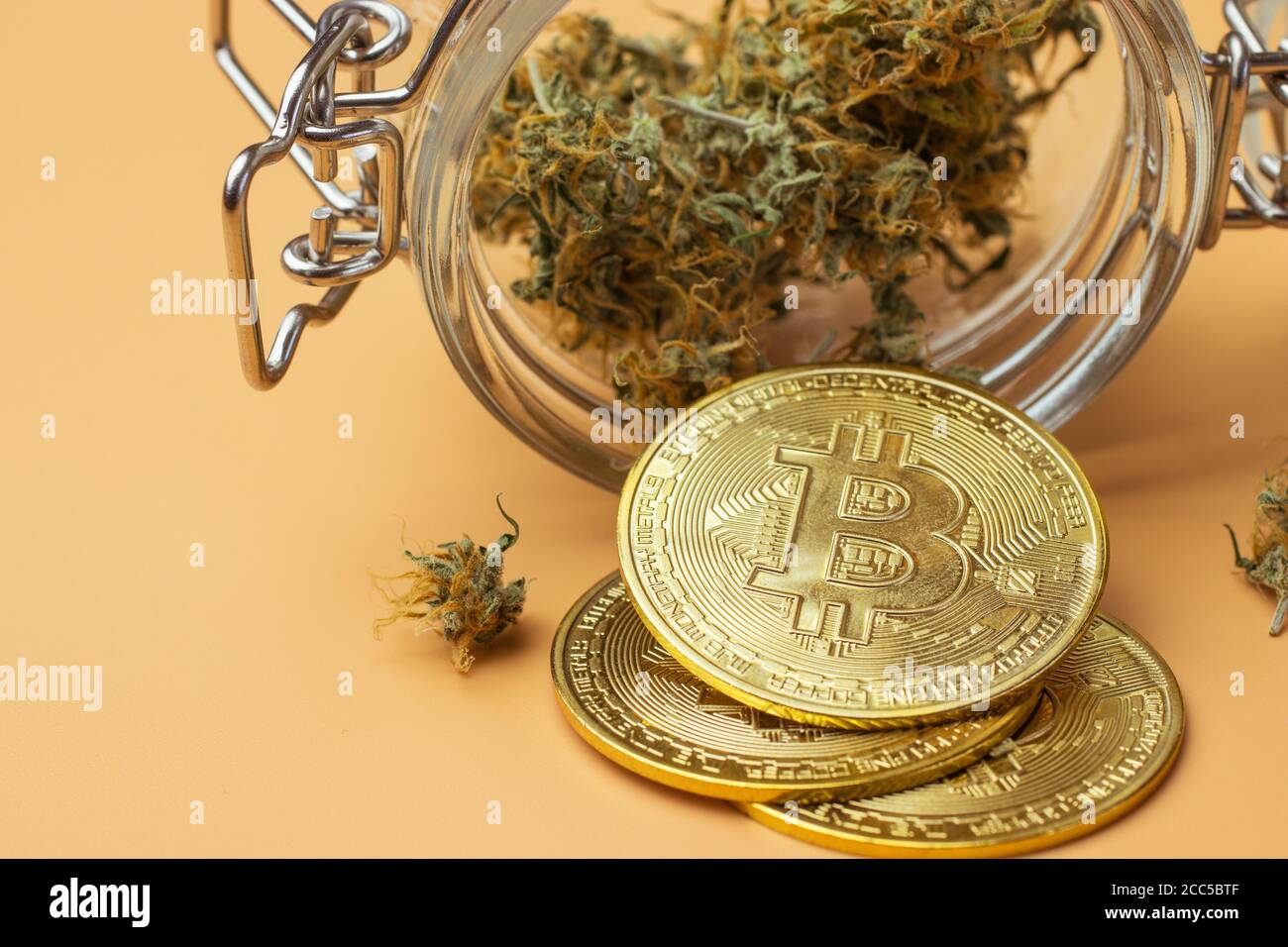 Bitcoin Münze neben Cannabis Knospen im Glas, Marihuana auf orangefarbenem Hintergrund Stockfoto