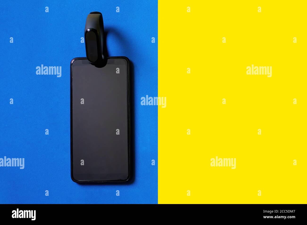 Klassischer blauer Fitness Tracker und Smartphone auf gelbem und blauem Hintergrund. Fitness Armband für das Sporttraining. Stockfoto