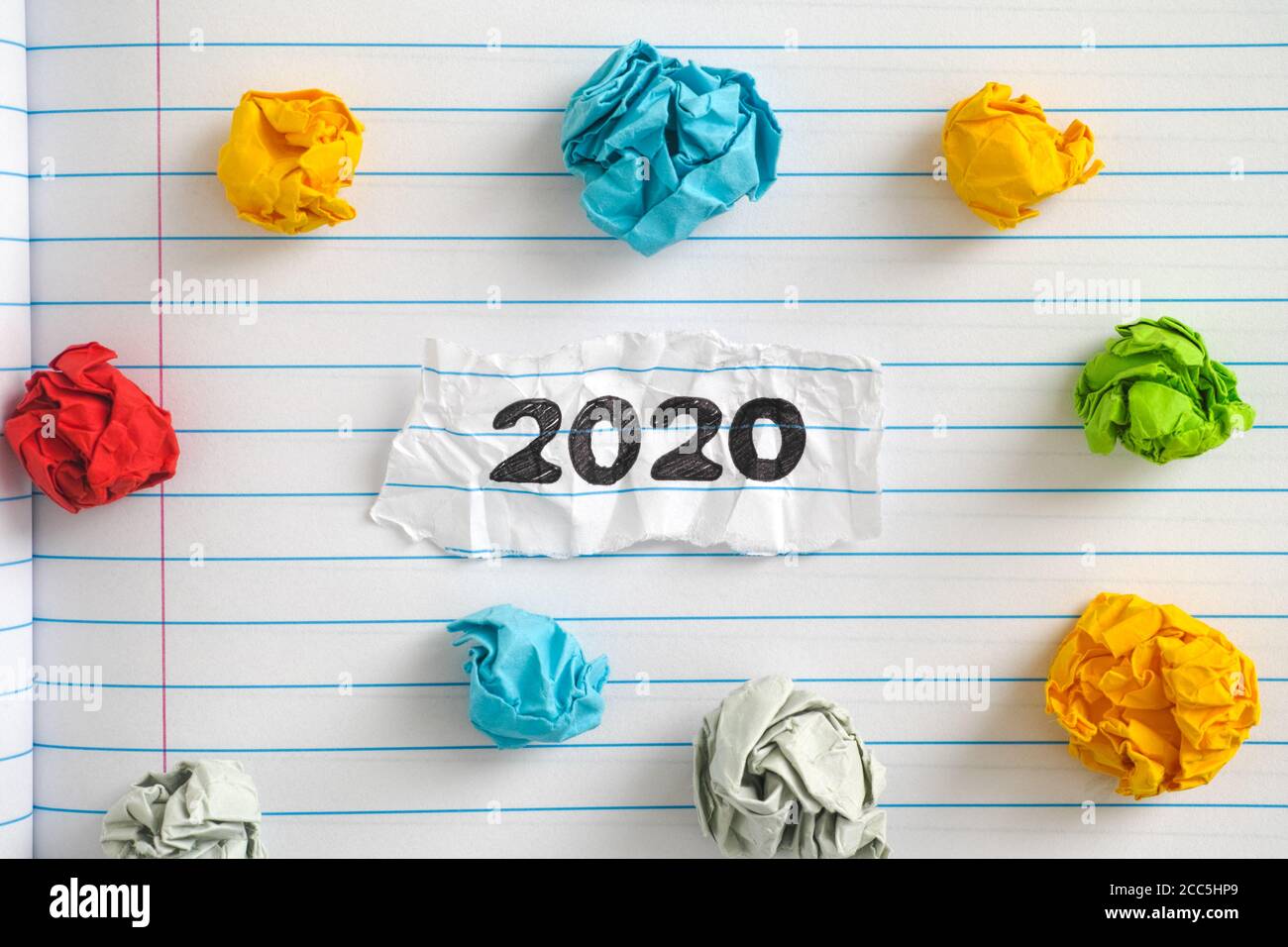 Das Jahr 2020. Ein Stück Papier mit dem Jahr 2020 darauf auf einem Notizbuch Blatt mit einigen bunten zerknitterten Papierkugeln um ihn herum geschrieben. Nahaufnahme. Stockfoto