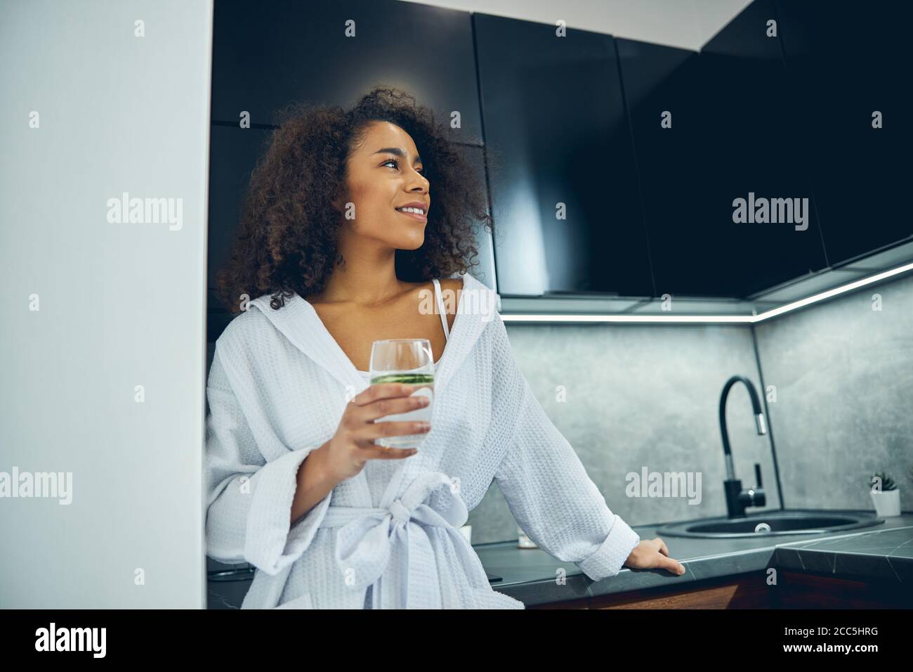 Lächelnde Frau, die sich auf die Küchenarbeitsfläche lehnte Stockfoto