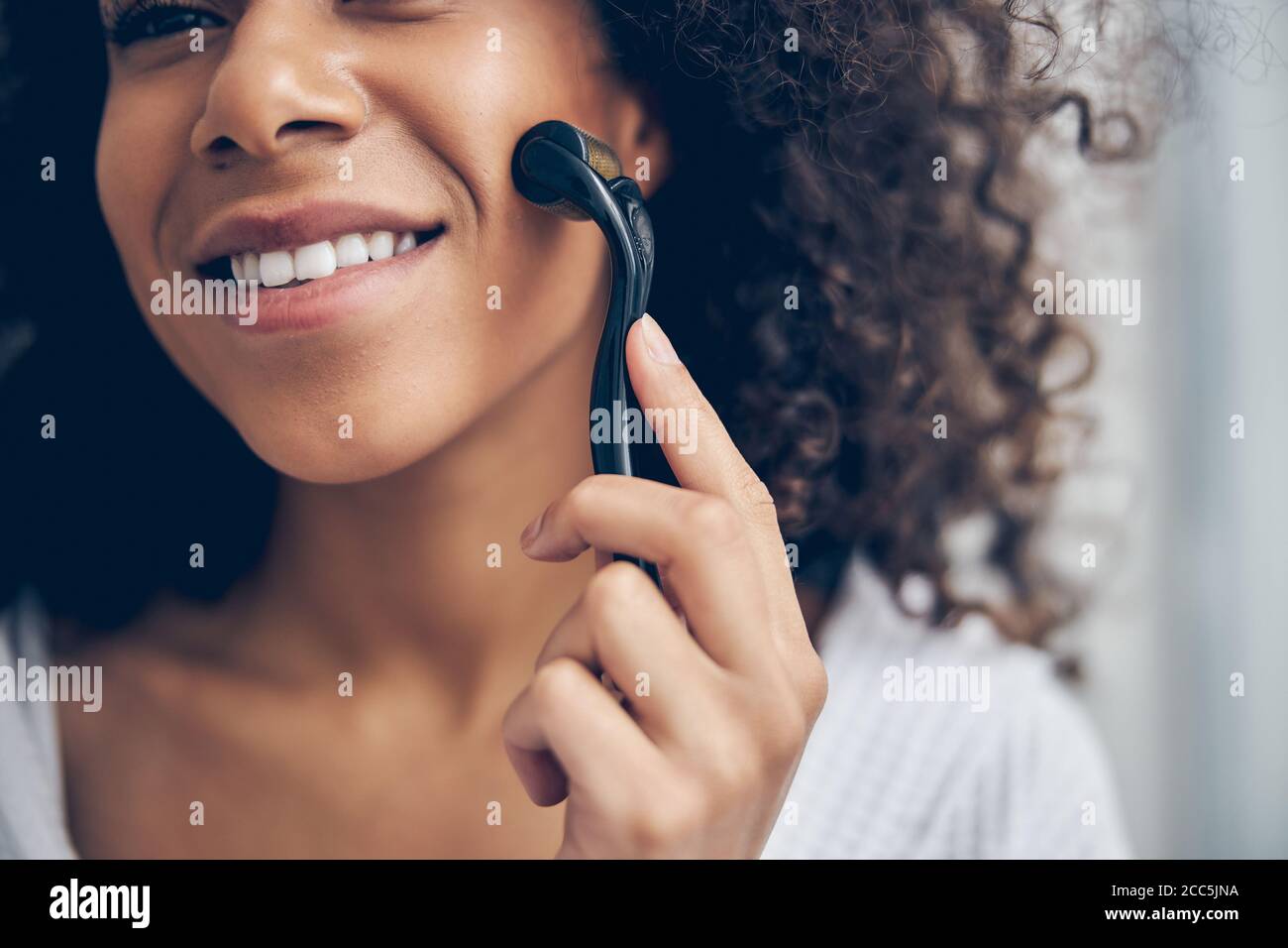 Frau massiert ihre Wange mit einer Mikro-Nadelrolle Stockfoto