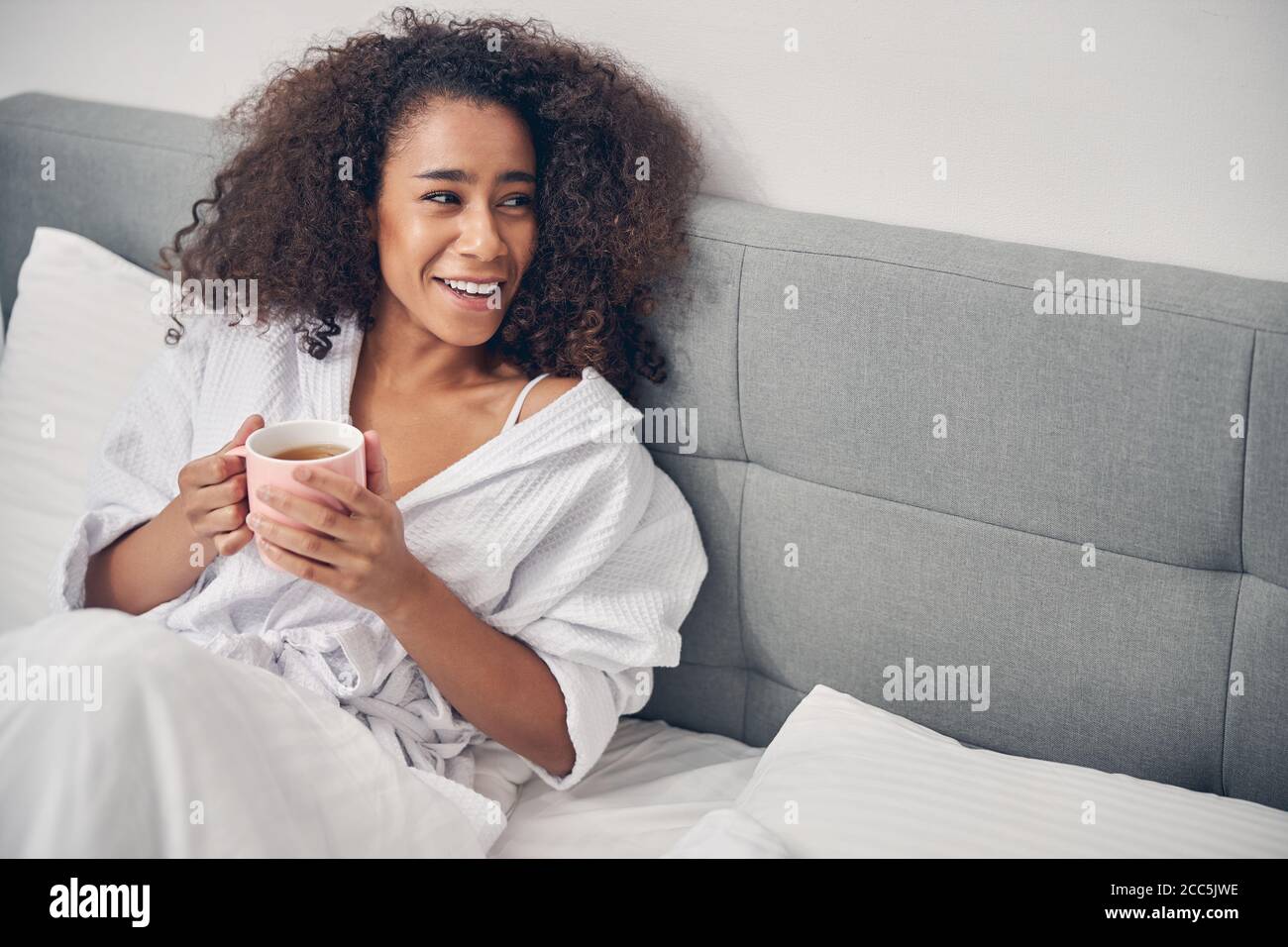 Fröhliche afroamerikanische Frau, die im Bett sitzt Stockfoto