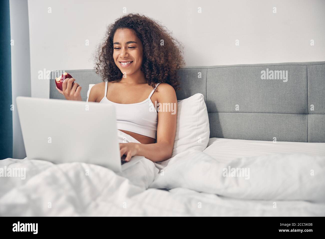 Lächelnde Frau mit ihrem Computer im Bett Stockfoto