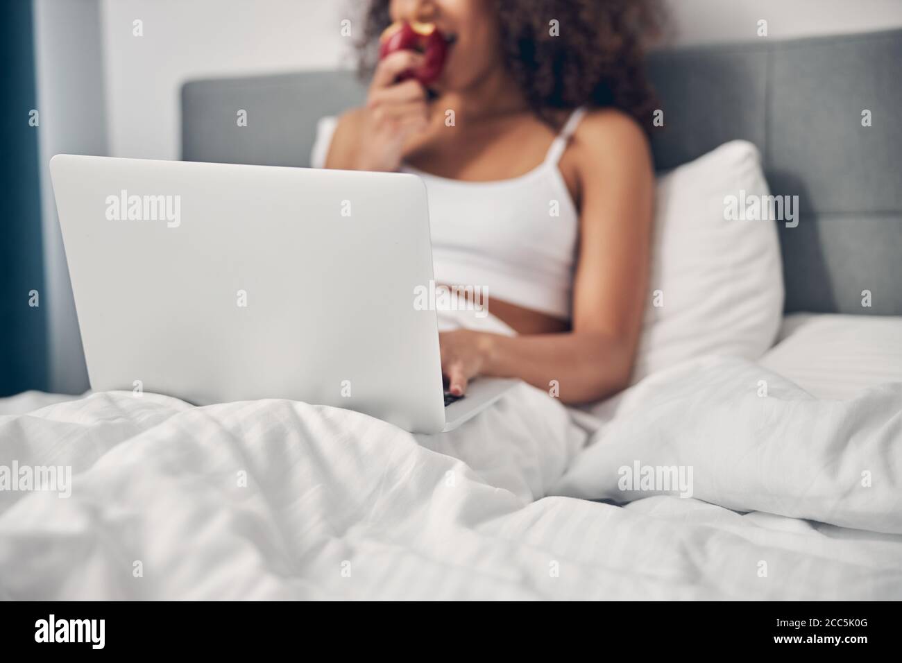 Lockiges Weibchen, das einen Apfel im Bett isst Stockfoto