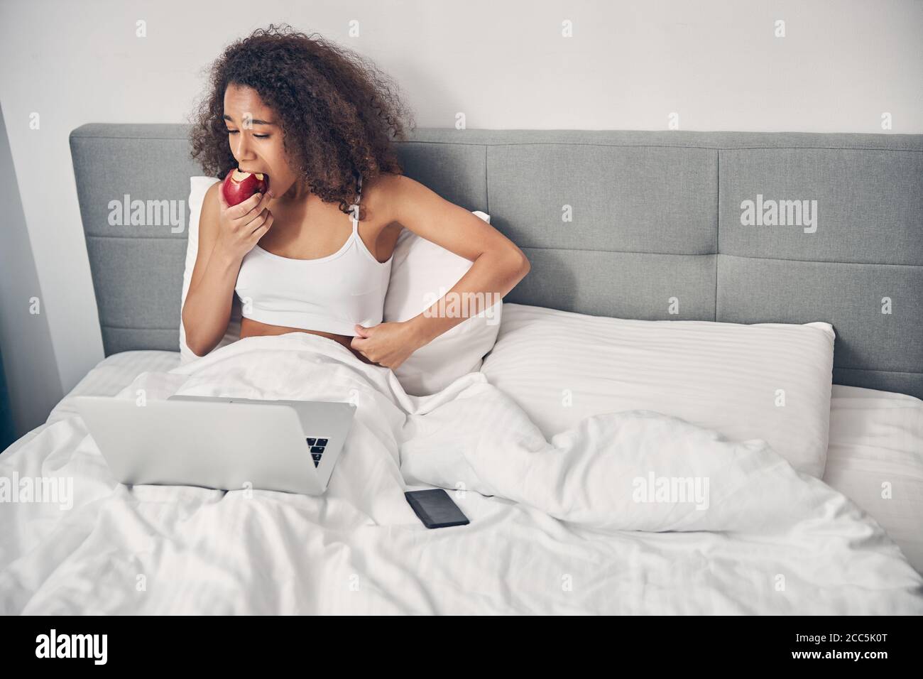 Dunkelhaarige Dame in einem Oberteil, das im Bett sitzt Stockfoto