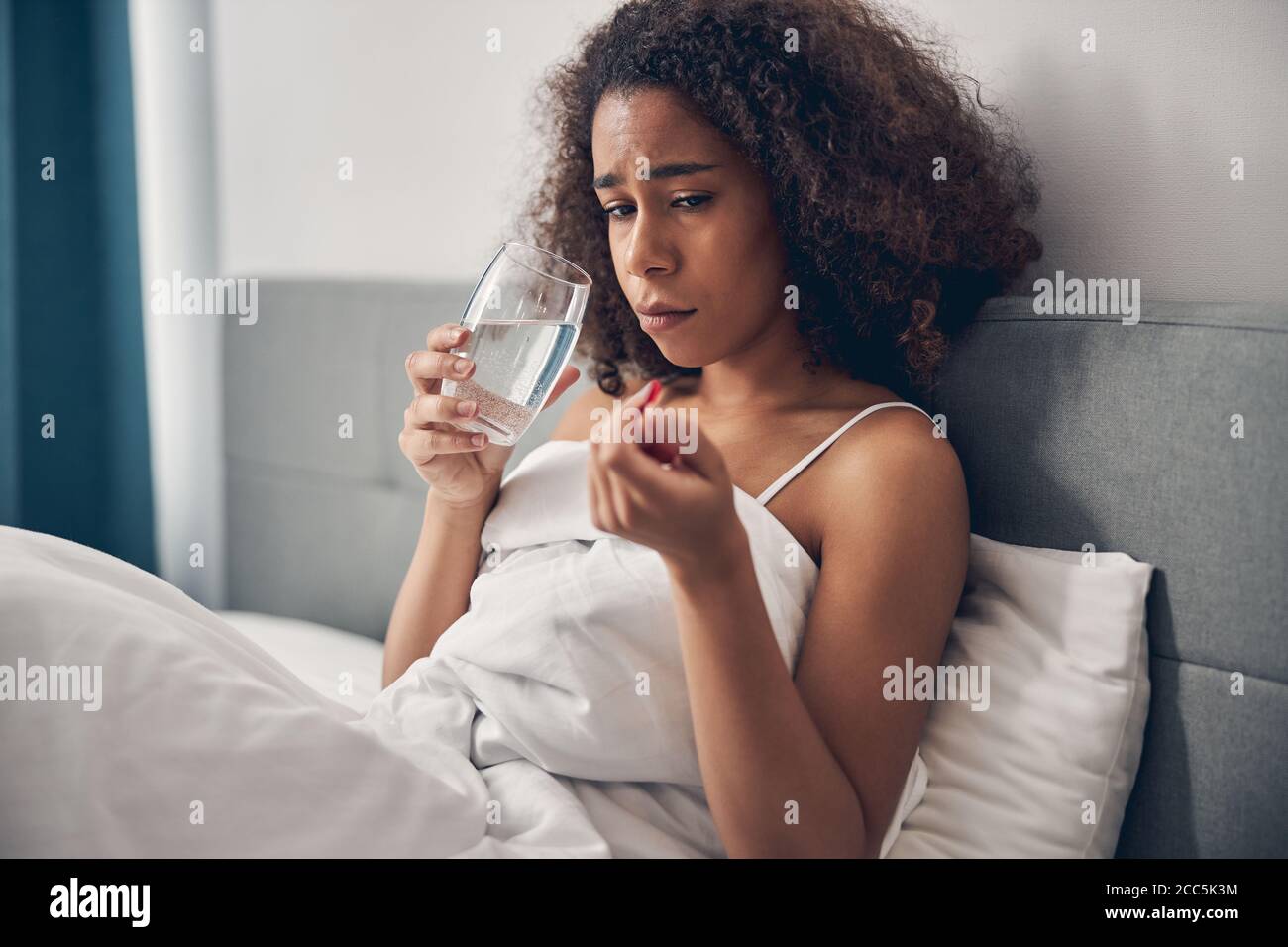 Kranke niedergelaunte junge dunkelhaarige Dame, die im Bett sitzt Stockfoto