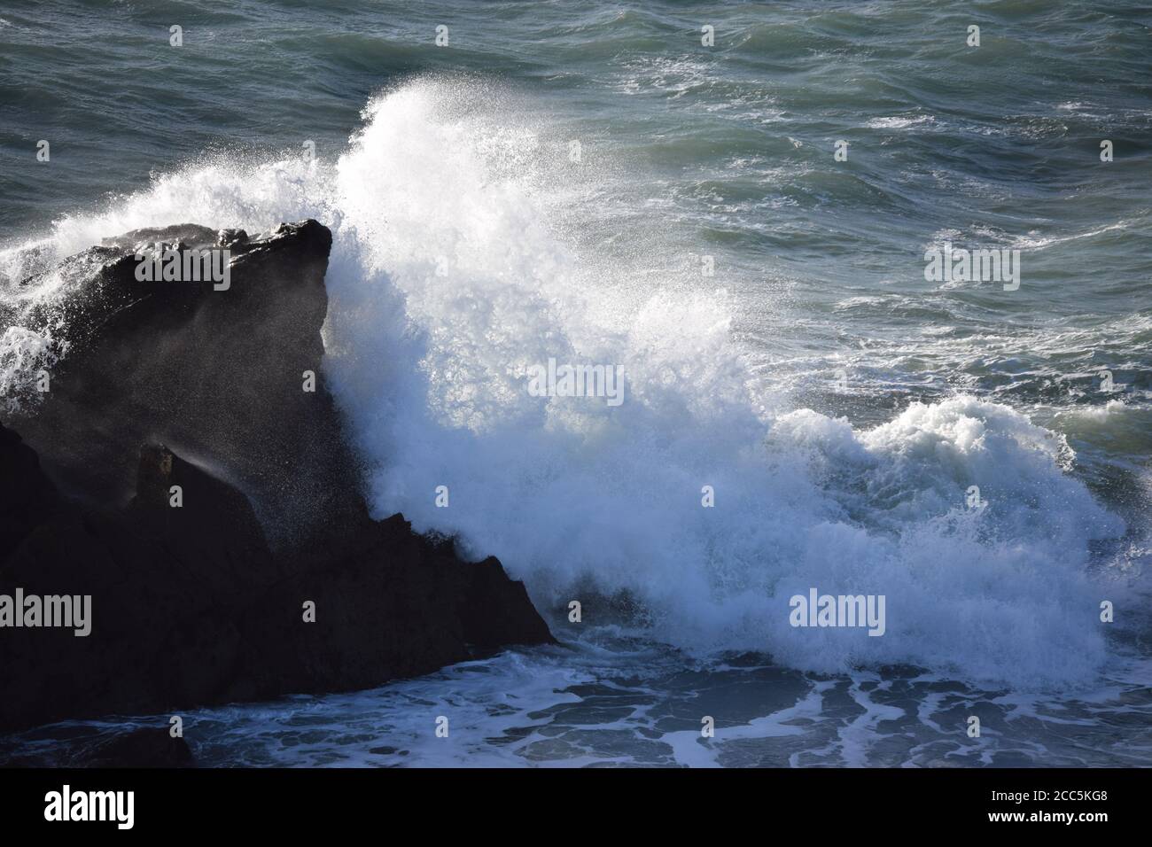 Die sonnenbeschienenen Wellen brechen auf den Felsen Stockfoto