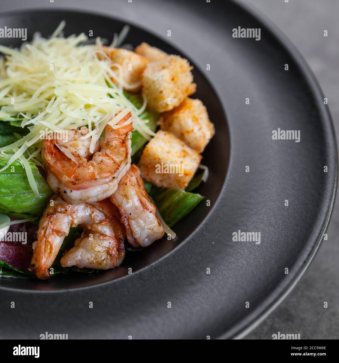 Caesar Salat mit Garnelen auf schwarzem Teller Stockfoto