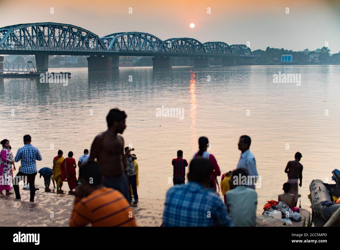 Hinduistische Pilger am Dakshineswar Ganga Ghat entlang des Hooghly Flusses mit der Vivekananda Setu Brücke im Hintergrund in Kolkata (Kalkutta), Indien. Stockfoto