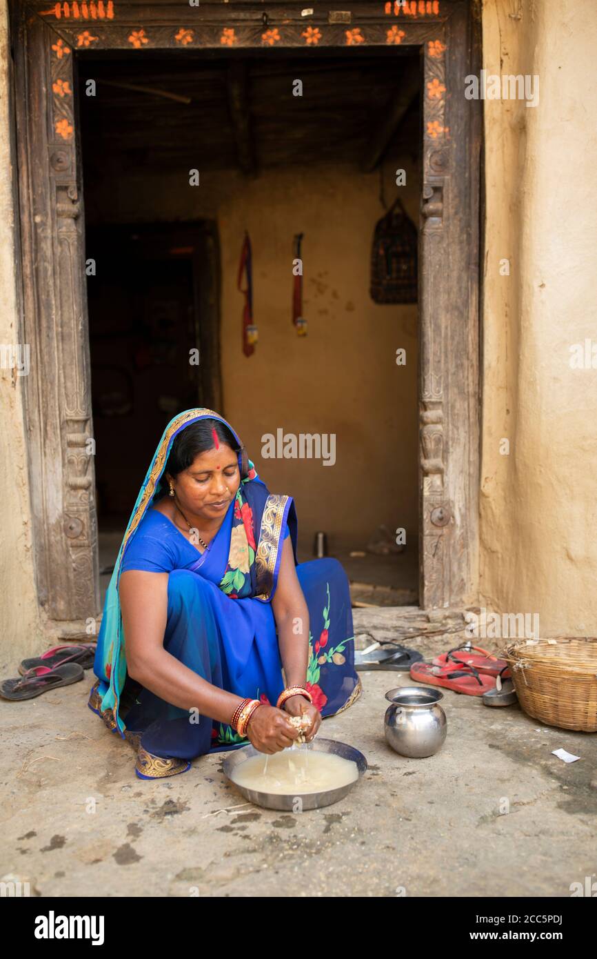 Eine Frau in einem traditionellen blauen Sari-Kleid wäscht ihr Reiskorn, bevor sie es vor ihrer Tür im ländlichen Bihar, Indien, Südasien, kocht. Stockfoto