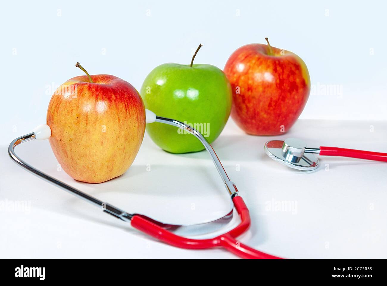 Vielfalt an frischen Äpfeln mit medizinischem Stethoskop auf weiß Stockfoto
