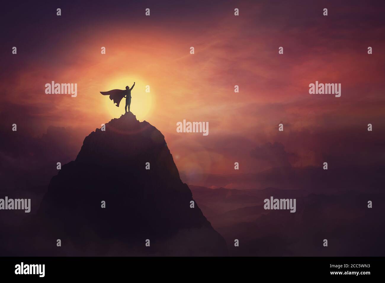 Konzeptuelle Sonnenuntergangsszene, Superheld mit Umhang, der tapfer auf einem Berg steht, sieht am Horizont entschlossen aus, eine Hand als siegreichen Anführer hochzuheben. Stockfoto