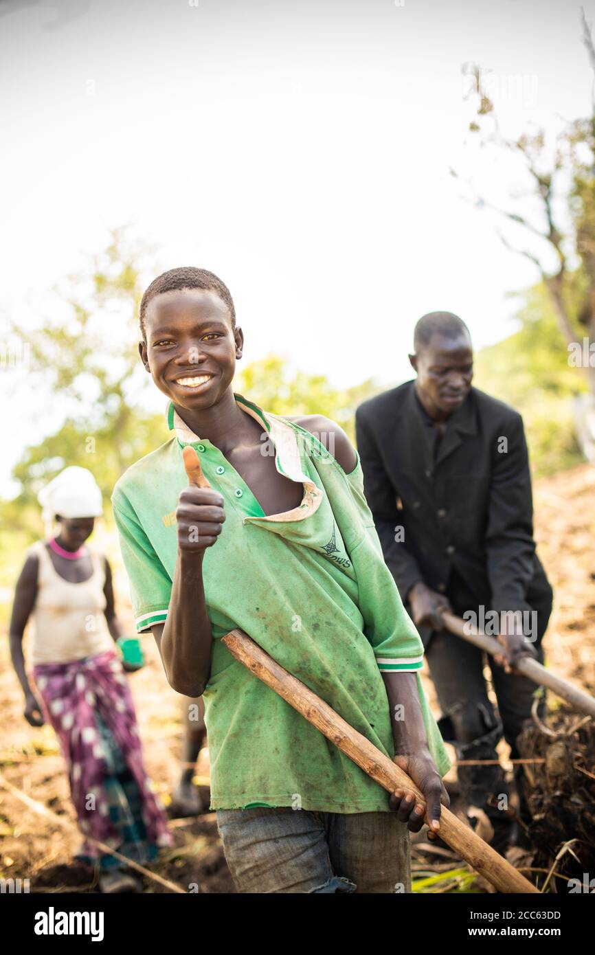 Ein junger Bauer hält eine Hacke, während er auf seinem Feld in der Palabek Flüchtlingssiedlung im Norden Ugandas, Ostafrika, arbeitet. Stockfoto