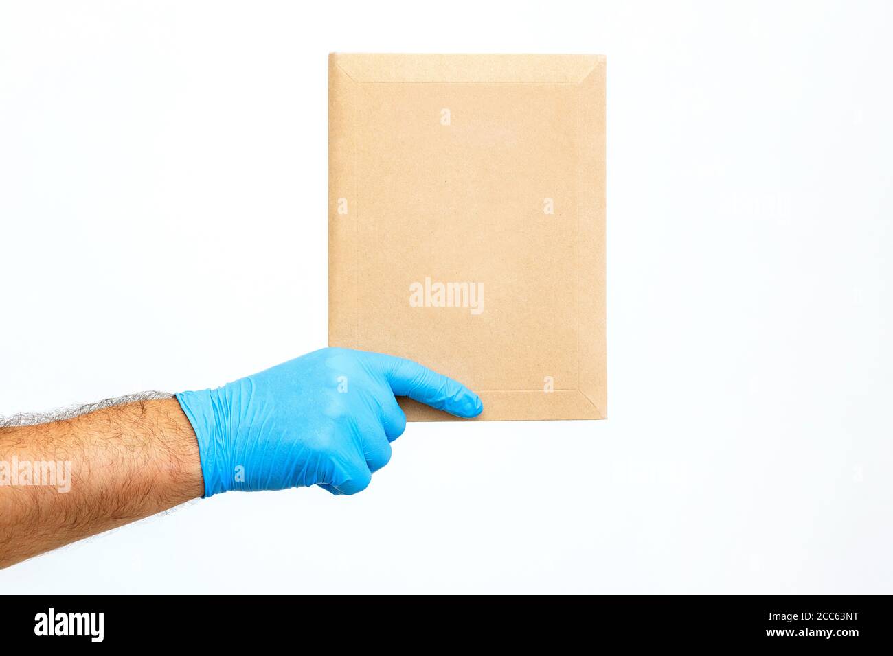 Nahaufnahme DIE Hand EINES männlichen Kurierers in einem medizinischen Handschuh hält einen Umschlag auf weißem Hintergrund. Hand Of Mailman Postversand. Paketversand Stockfoto