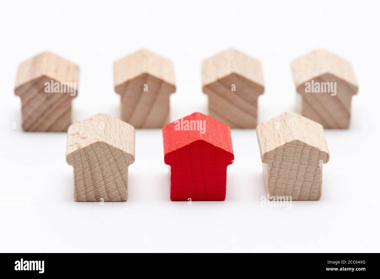 Winzige Holzspielzeughäuser in zwei Reihen, das in der Mitte rot bemalt, weißer Hintergrund Stockfoto