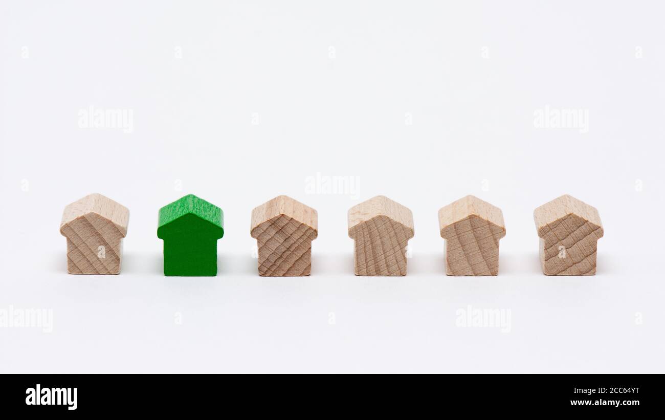 Winzige Holzspielzeughäuser in einer Reihe, eines davon mit grünem, weißem Hintergrund Stockfoto