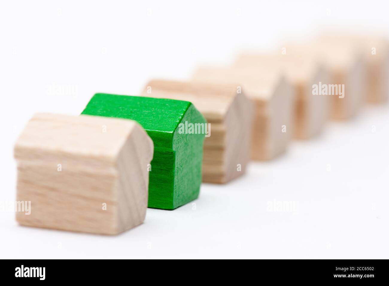 Winzige Holzspielzeughäuser in einer Reihe, eines davon mit grünem, weißem Hintergrund Stockfoto