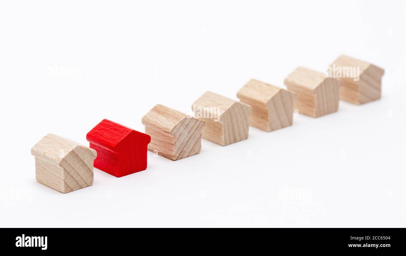 Winzige Holzspielzeughäuser in einer Reihe, eines davon mit rotem, weißem Hintergrund Stockfoto
