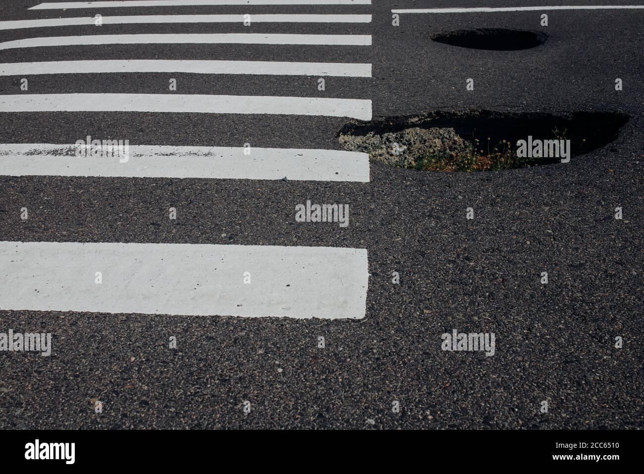 Gefährliche Löcher auf einer asphaltierten Autobahn in der Nähe einer Fußgängerüberfahrt. Straßensperrung. Die Notwendigkeit einer dringenden Reparatur der Fahrbahn Stockfoto