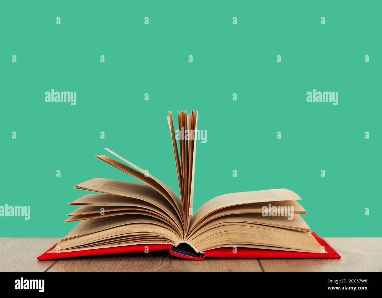 Öffnen Sie das Buch Lehrbuch in einem roten Umschlag auf einem Holzschreibtisch mit mintgrünem Hintergrund. Zurück zur Schule Abstand zu Hause Bildung.Quarantine Konzept des Aufenthalts zu Hause Stockfoto