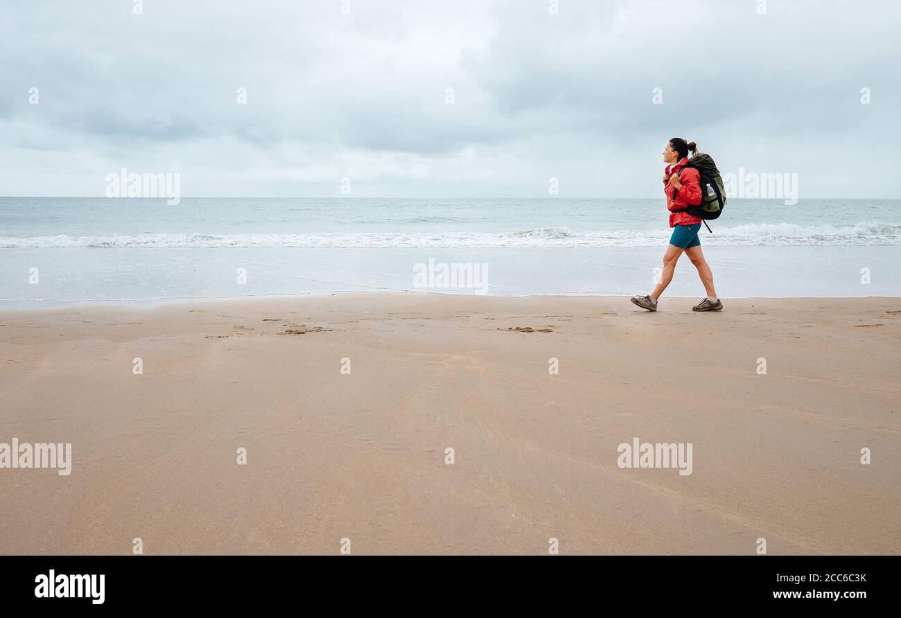 Frau Reisende gehen an regnerischen Tagen auf leerem Meeresstrand Stockfoto