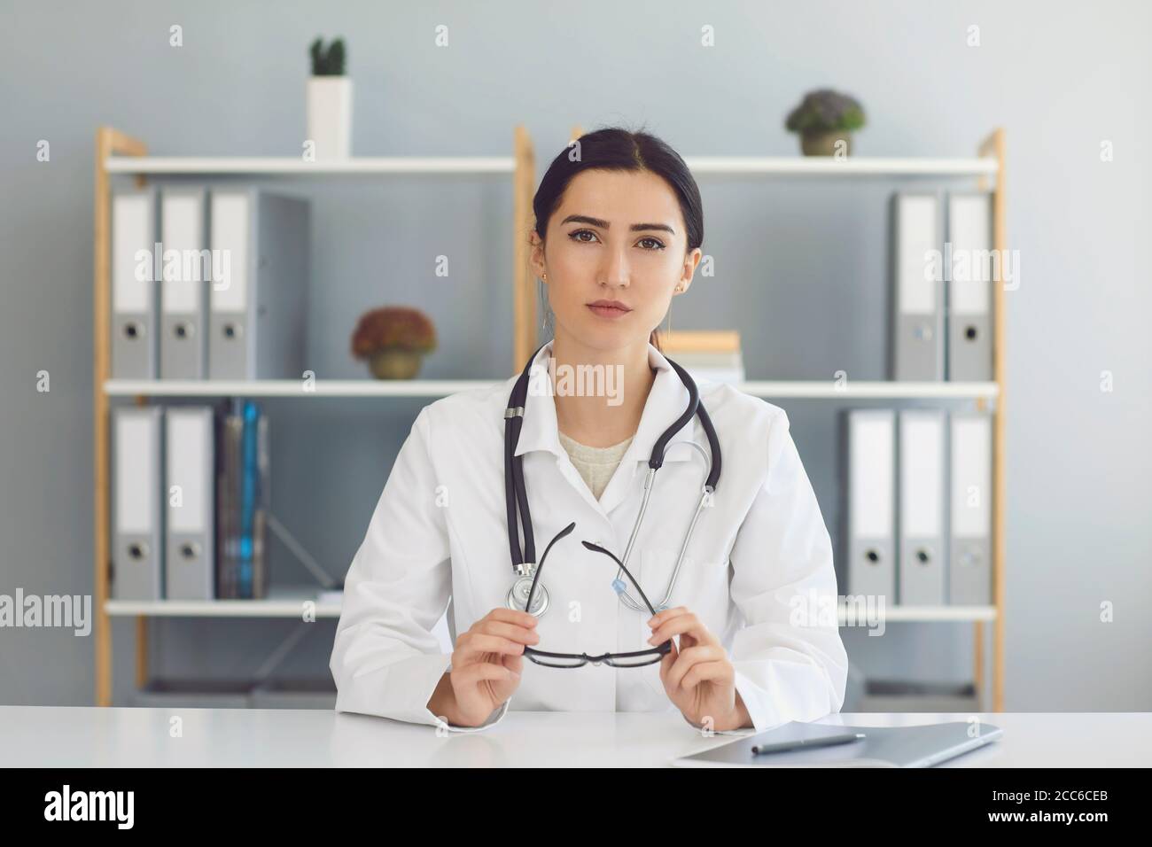 Frau Arzt sitzen und Blick auf die Kamera in der Klinik Büro Online Stockfoto